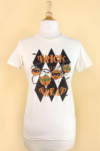 ivory short sleeved t shirt with an illustration of 4 jack-o’-lanterns wearing masks surrounded by bats in front of a harlequin diamond pattern with the message “TRICK OR TREAT” written in orange capital letters. Seen on a dress form