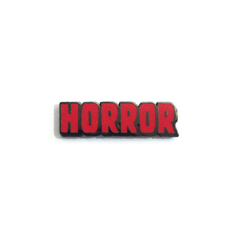Red enameled pin on pewter colored metal “HORROR” in all capital letters