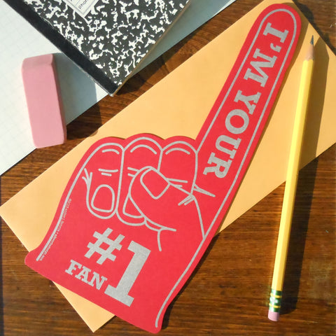 Die cut red greeting card in the shape of a novelty foam finger, with “I’m Your #1 Fan” written in grey