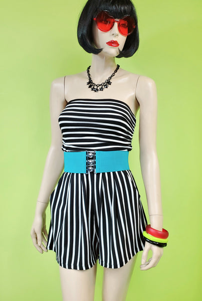 A mannequin wearing a strapless black and white striped romper accessorized with a teal blue elastic belt. It has slight ruching at the bodice and relaxed fit style high-waisted shorts.