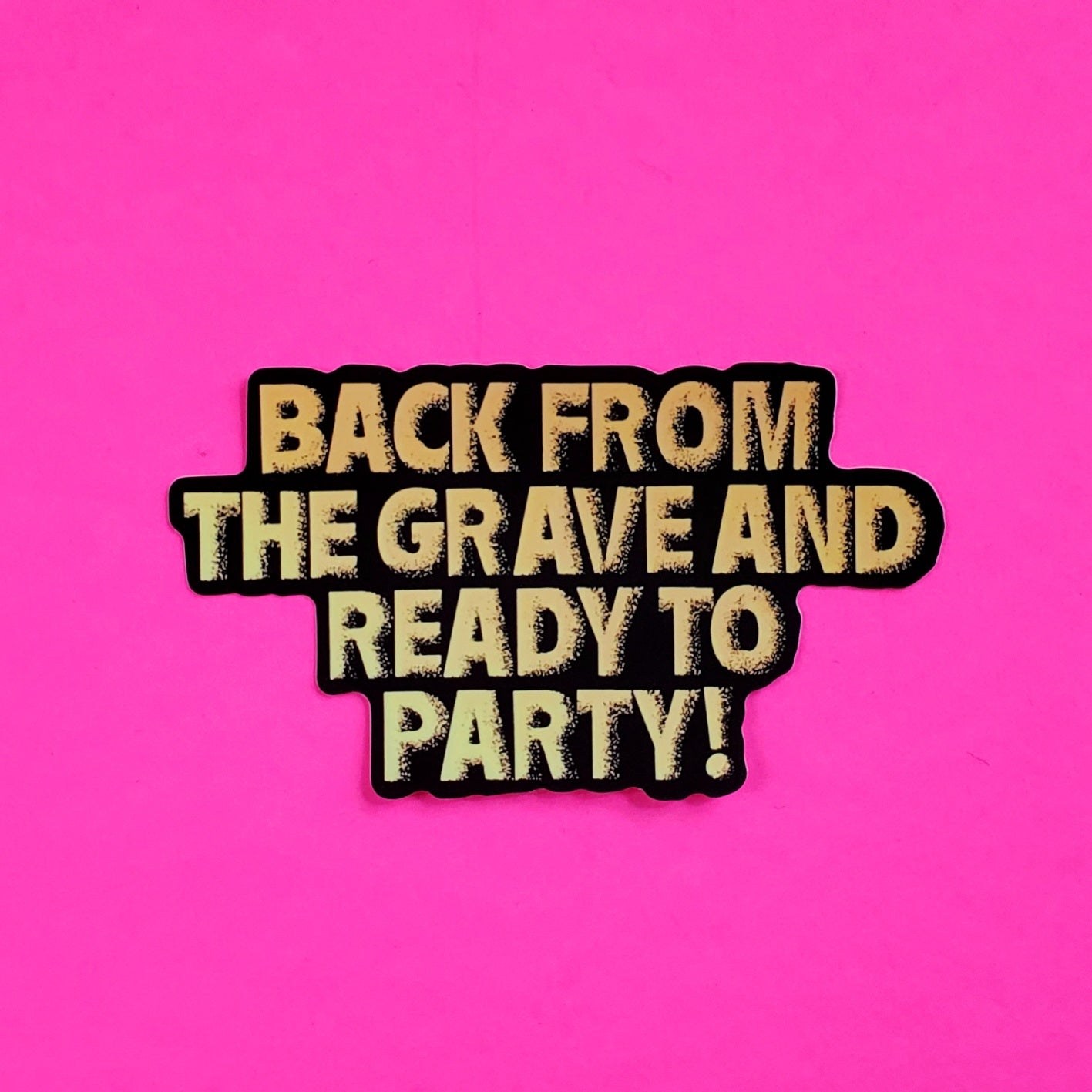 gold lamé woven patch printed with the tagline from the 80s cult zombie movie The Return of the Living Dead: “BACK FROM THE GRAVE AND READY TO PARTY!” written in gold lamé on a black background with gold lamé border