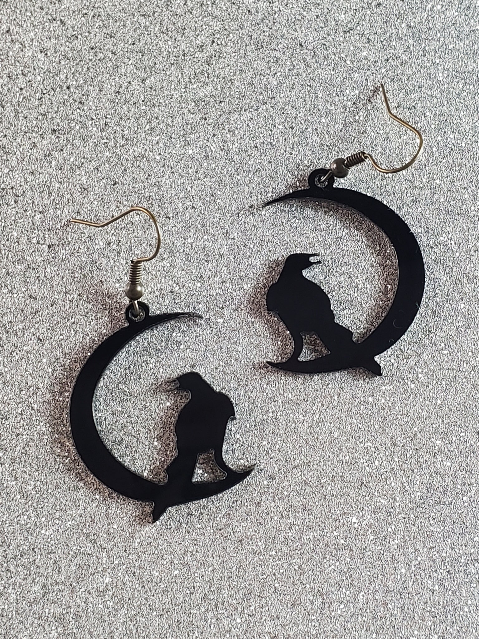 Laser cut acrylic dangle earrings in the shape of a crow perched on a crescent moon. Shown laying flat