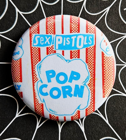 1.25” round pinback button of red and blue “Sex Pistols Pop Corn” illustration on white background 