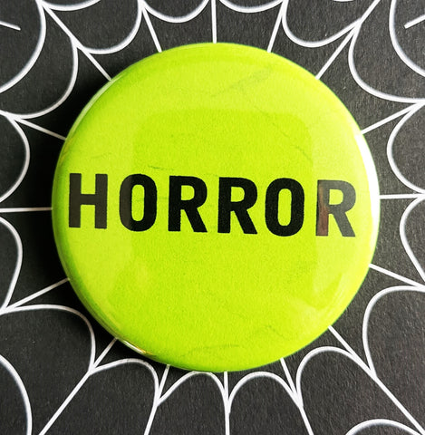 1.25” round button reading “HORROR” in black on a neon green background 