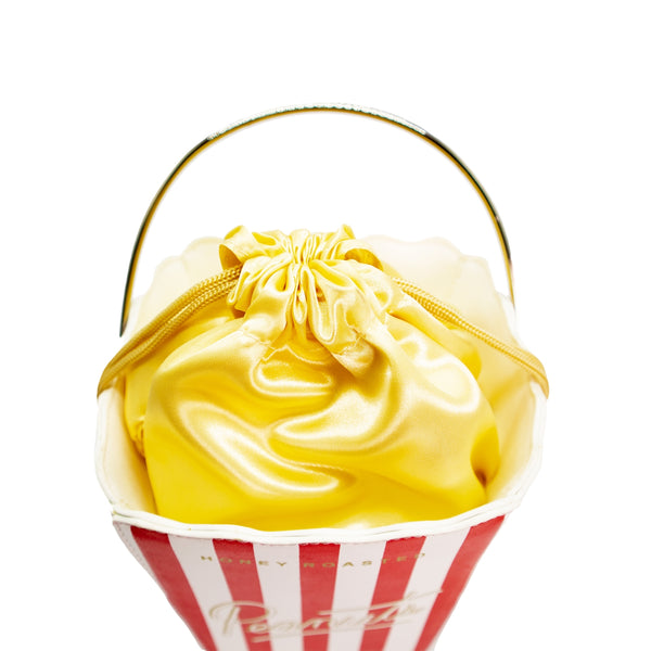 Novelty purse in the shape of a box of red and white striped popcorn. Shown from top to display yellow satin drawstring “popcorn” and metal handle