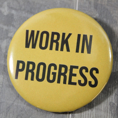 2.25” round pinback button “WORK IN PROGRESS” written in black capital letters on a yellow background 