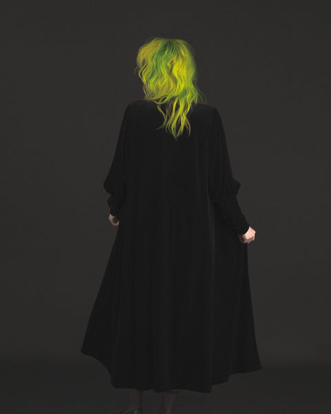Model wearing black velvet duster with bow tied detail at the collar, slightly gathered shoulders, and Juliet sleeves. Shown from the back