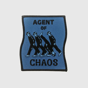 A warped rectangular shaped embroidered patch with a navy blue background and black border. Message of “AGENT OF CHAOS” with illustration of four men wearing suits and hats walking to the left with one walking upside down in the opposite direction 