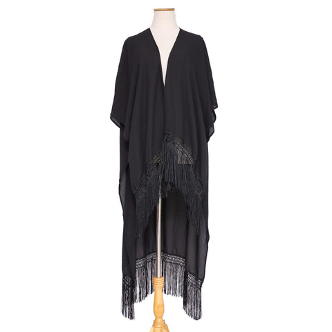 A dress form wearing a black open front cover-up with black fringe detail at the high-low hem. Shown in full length shot