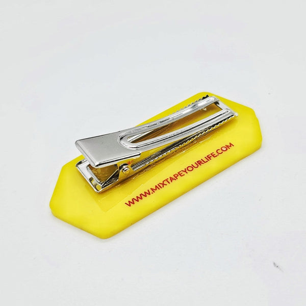Laser-cut acrylic hair clip in the shape of a yellow stick of butter with black and red painted label details. Shown from the back
