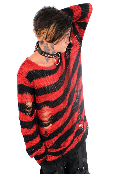 Model wearing an open knit oversized sweater with black and red stripes and distressed detail at the sleeve and body. Shown from the side