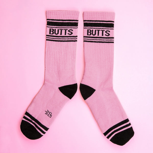Pink crew socks with black striped cuffs and toes with “BUTTS” written in black. Shown flat side by side