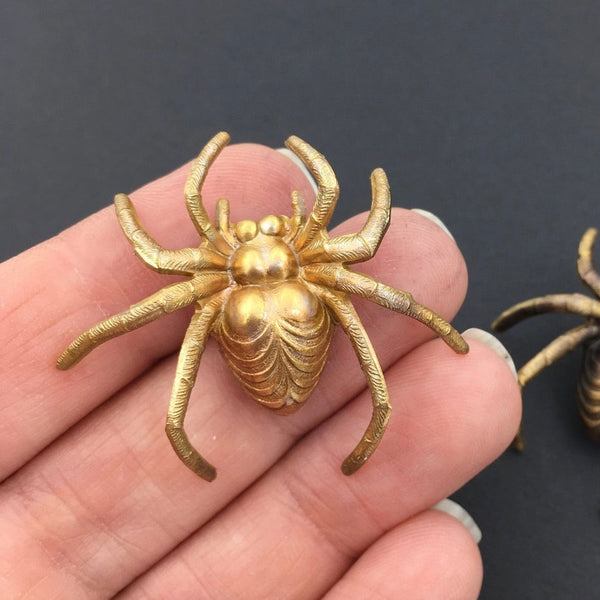 Brass spider shaped brooch with a matte bright gold finish, held in a hand to show size 