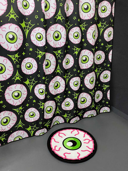 fabric shower curtain with an all-over neon pink and green bloodshot eyeball print on a black background. Shown with matching bath mat