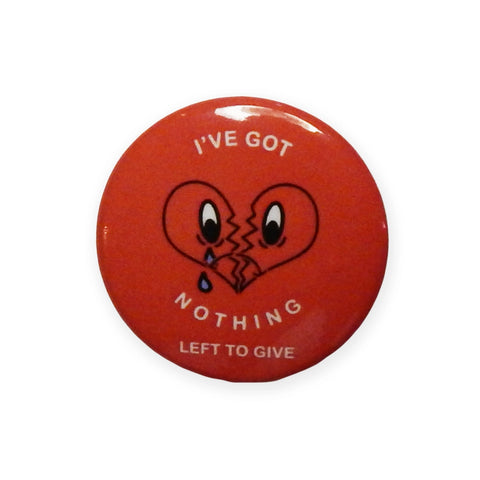 A round pinback button with an illustration of a broken heart with a frowning and crying face, surrounded by the words “I’VE GOT NOTHING LEFT TO GIVE” written in small white letters