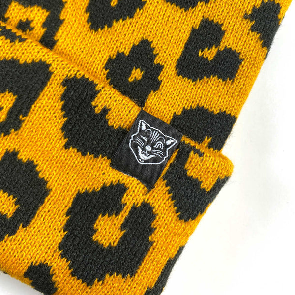 black and orange leopard print (with subtle bats in the pattern) knit hat with a set of pointy little matching cat ears on top. Shown up close with Sourpuss logo tag