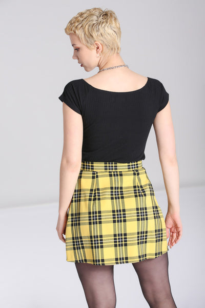 Model wearing a black and yellow tartan print pleated miniskirt with a faux wrap detail in the front. It has a black faux leather strap at the left hip of the waistband with a shiny silver heart shaped buckle. Shown from the back
