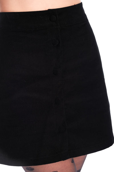 black corduroy button-front full a-line skirt in a above the knee length with side seam pockets. Shown on a model wearing patterned tights in close up