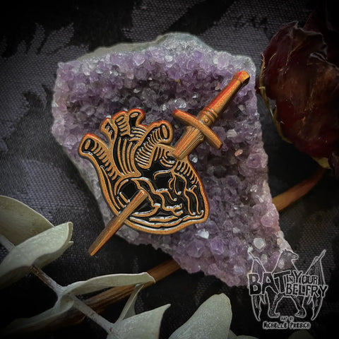Bronze tone metal hard enamel pin with black detailing of an anatomical style heart with a 3D dagger through it