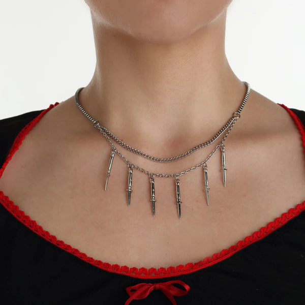 Silver metal box and link double chain necklace with 6 vertically hanging switchblade pendants on the box chain. Shown in close up worn by a model 