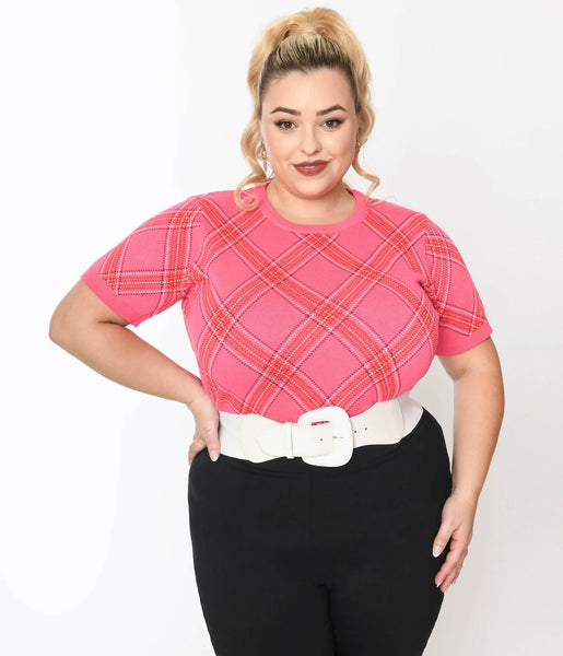 A plus size model wearing a crew neck pullover sweater with short sleeves in a pink, red, and white bias plaid pattern. It has a wide ribbed waistband. Shown from the front and worn with a white belt tucked in