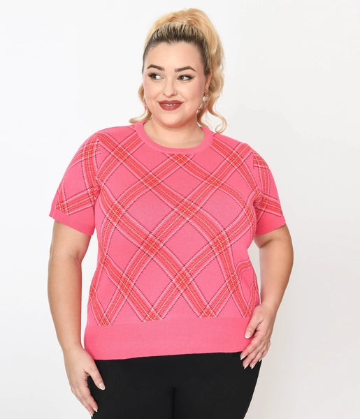 A plus size model wearing a crew neck pullover sweater with short sleeves in a pink, red, and white bias plaid pattern. It has a wide ribbed waistband. Shown from the front untucked