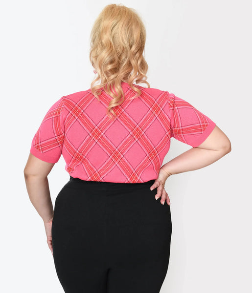 A plus size model wearing a crew neck pullover sweater with short sleeves in a pink, red, and white bias plaid pattern. It has a wide ribbed waistband. Shown from the back tucked in 
