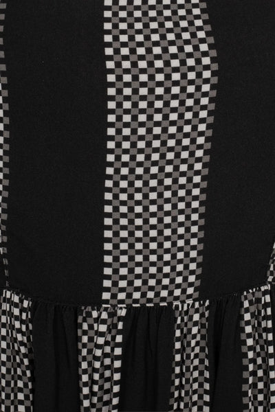 sleeveless dress in a grey and black checker plaid pattern with alternating wide black vertical straps. It has wide adjustable self straps with O-ring detail connecting them to the dress. The dress has princess seaming, a shallow scoop neckline, and a full gathered skirt that ends below the knee. Shown in close up of pattern