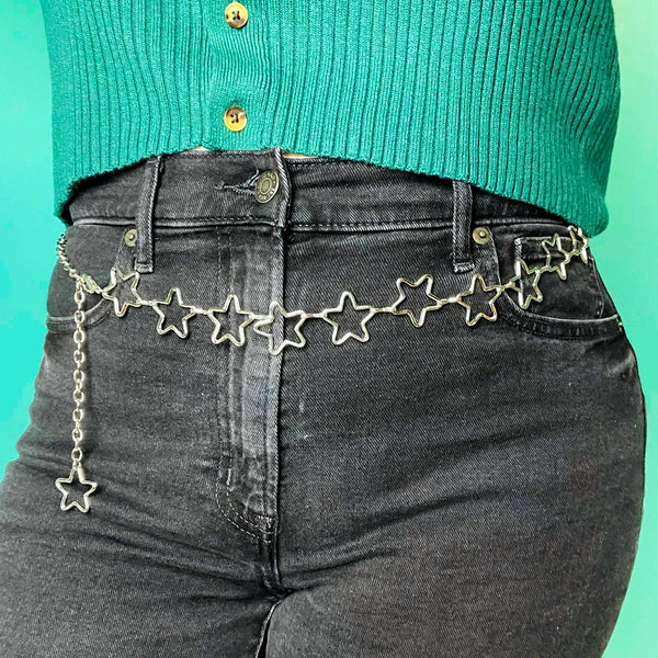 Silver metal chain belt with row of silver stars and link chain with lobster claw closure. Seen worn by a model from the waist down 
