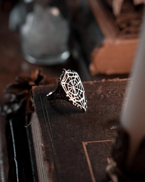 stainless steel ring on in the shape of a shield-like spider web with openwork design and scalloped edges. Shown resting on an antique book to display band