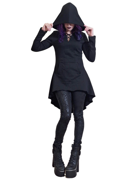 Model wearing black French Terry hoodie with feature neckline, long sleeves with thumb holes, a kangaroo pocket, oversized black hood (shown up), and a flared high-low hemline. Shown in full length shot