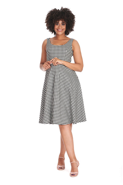 A model wearing a black and white gingham pattern sleeveless fit and flare dress. It has a slightly scooped neckline, princess seaming, side seam pockets, and a skirt that ends just below the knee. Shown from front