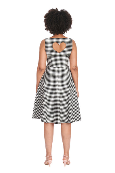 A model wearing a black and white gingham pattern sleeveless fit and flare dress. It has a slightly scooped neckline, princess seaming, side seam pockets, and a skirt that ends just below the knee. Shown from back to display heart-shaped keyhole detail at the back of the bodice 