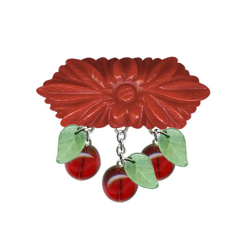 Hexagonal red retrolite carved flower brooch with three sets of red and green glass cherry and leaf beads attached at the bottom