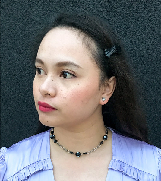 Choker necklace made of silver plated link chain with alternating black star charms and black ball charms decorated with white stars. Shown worn by model