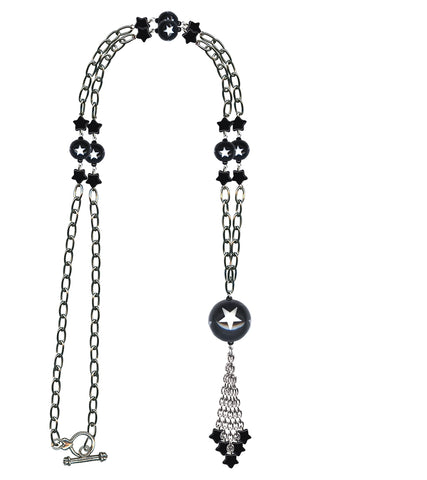 A long silver plated link style chain necklace with a toggle closure and alternating black star charms & black ball charms decorated with white stars. End of the necklace has a tassel made of matching chain with black star charms