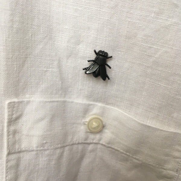 A brass house fly-shaped brooch with a shiny black finish. Shown on a white linen shirt