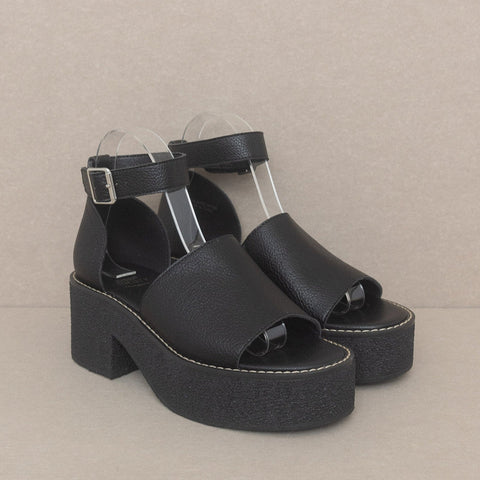 Black faux leather open toe platform sandals with matching ankle strap and silver metal buckle. Outsole is solid black textured rubber. Shown unworn from three quarter angle