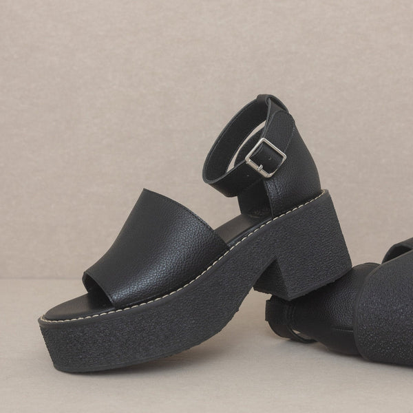 Black faux leather open toe platform sandals with matching ankle strap and silver metal buckle. Outsole is solid black textured rubber. Shown unworn from side