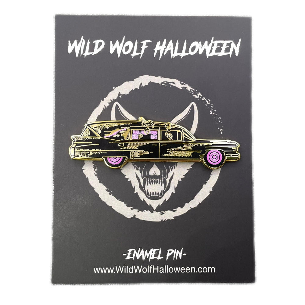A gold metal enamel pin with black details of a vintage style hearse with bright pink curtained windows and tires. Pictures a skeleton wearing a chauffeur’s hat in the passenger seat. Shown on its backing card