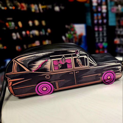 A novelty purse shaped like a vintage black hearse with brownish orange highlights and pink-curtained windows & tires. Has a skeleton wearing a chauffeur’s hat in the passenger’s seat