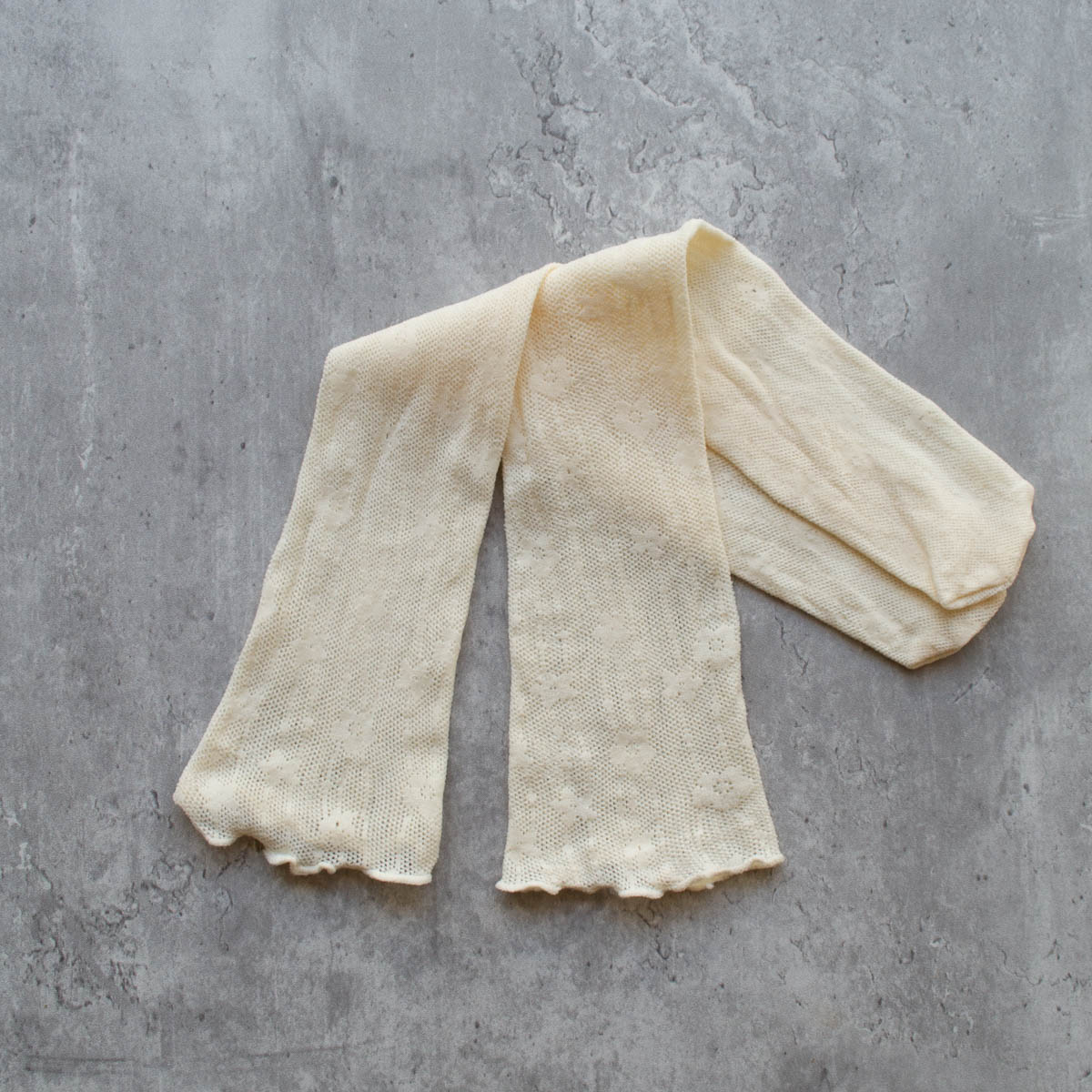 A pair of openwork knit socks in a creamy off white color with a striped floral pattern. Seen flat