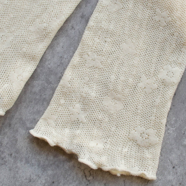 A pair of openwork knit socks in a creamy off white color with a striped floral pattern. Seen flat in close up