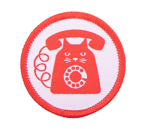 A woven round patch with embroidered bright red edge featuring an image of a bright red and white cat with rotary phone features on a white background
