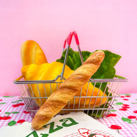 A novelty ballpoint pen with an exterior shape of a loaf of baguette bread. Shown on a checkerboard background against a pink wall.