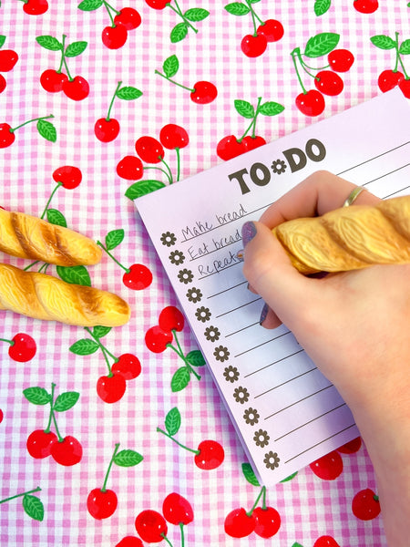 A novelty ballpoint pen with an exterior shape of a loaf of baguette bread. Shown being used to write a grocery list