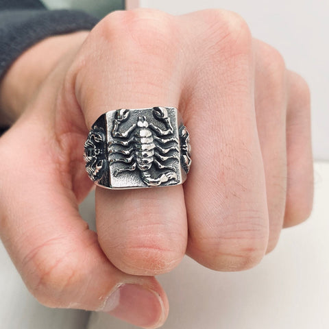 Hand wearing a square stainless steel ring with a highly detailed scorpion on three sides of the ring
