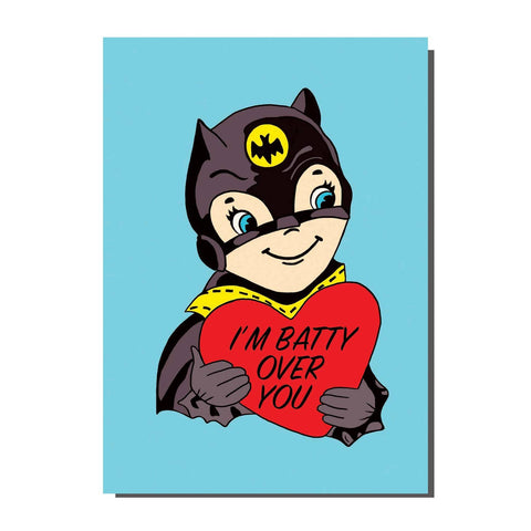 A rectangular note card with a vintage valentine style illustration of Batman holding a heart with the message “I’M BATTY OVER YOU” written inside. On a light blue background 