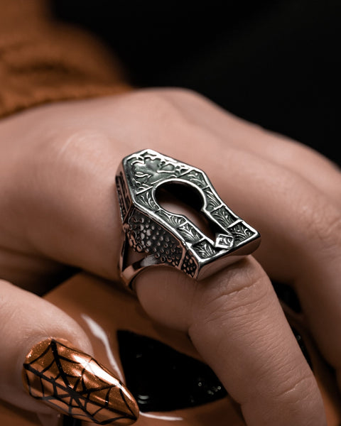 Model wearing large gravestone shaped stainless steel ring with filigree detailing and a keyhole detail in the middle. Shown from a left side angle in close up