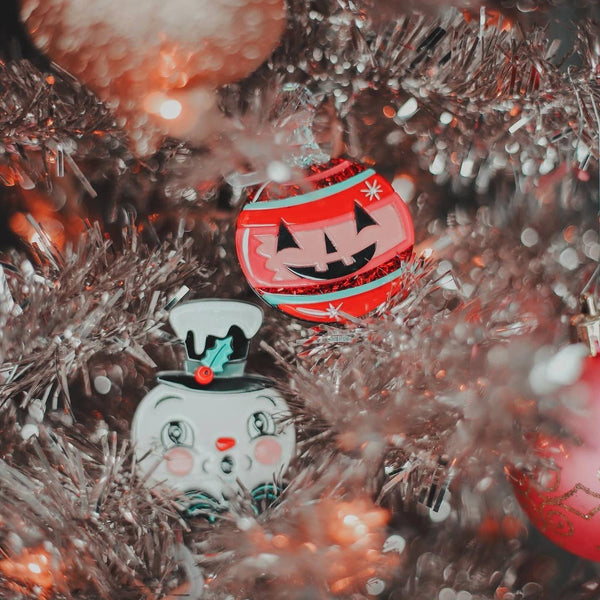 Spooktacular Sparkle Brooch by Johanna Parker x Lipstick & Chrome, tree ornament shaped brooch with black jack-o’-lantern face and green/red/pink stripes with red and iridescent glitter. Shown on a silver tinsel tree with Spooky Frosty brooch